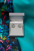 Silver earrings in a box on a colourful fabric background.