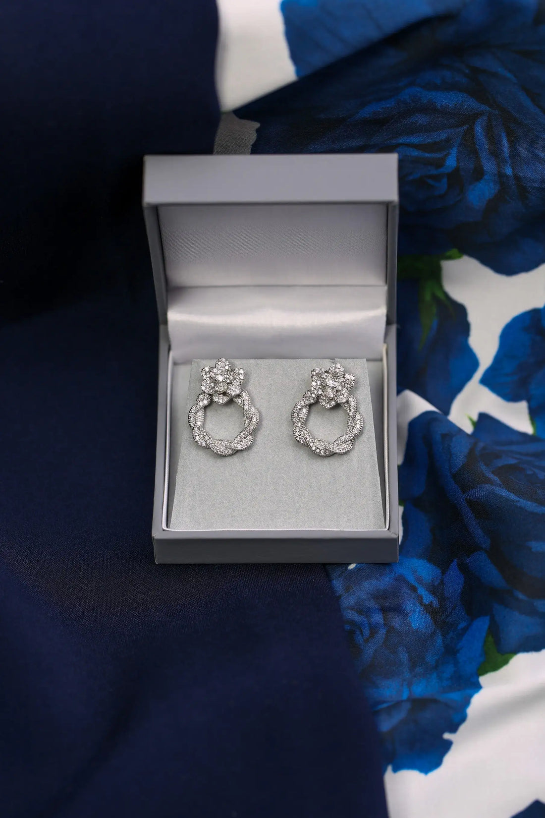 Silver earrings in a grey jewellery box on a blue fabric background