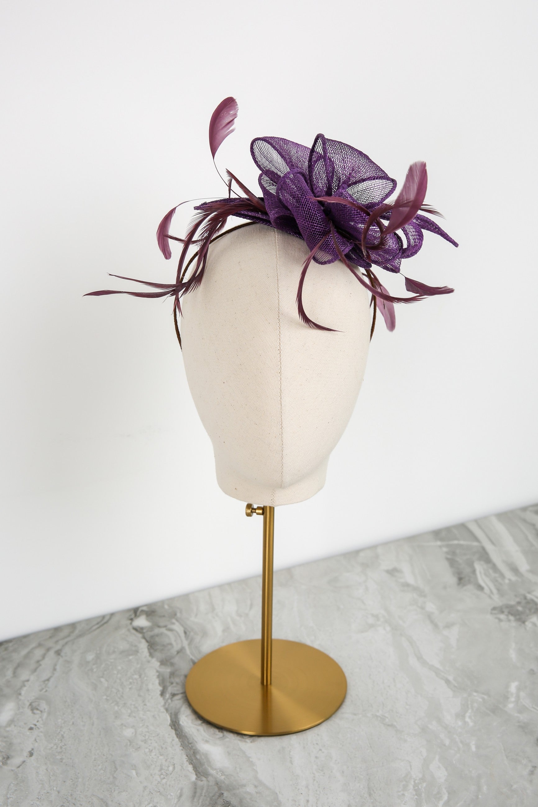 Purple feathered headpiece on a mannequin head against a white background