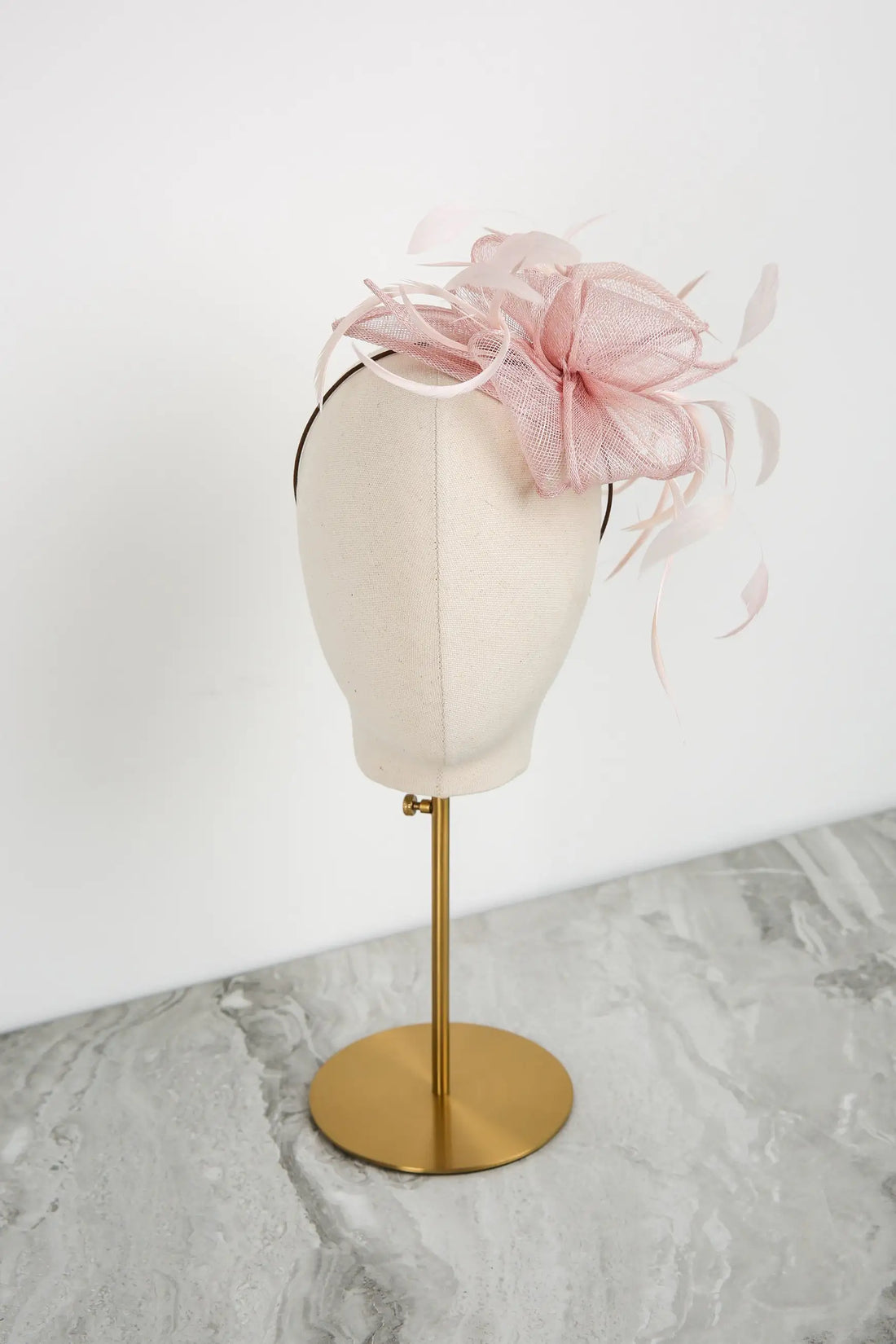 Pink fascinator on a mannequin head with a gold stand against a white background
