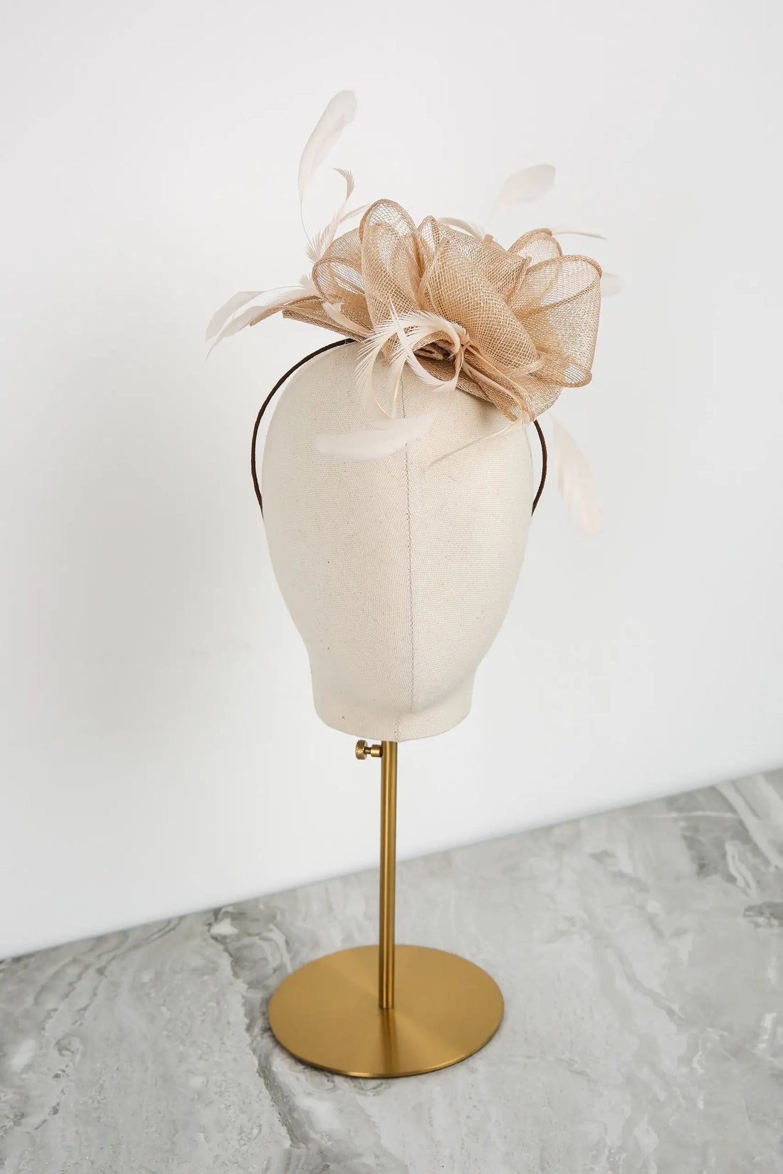 Beige fascinator on a mannequin head with a gold stand against a white background