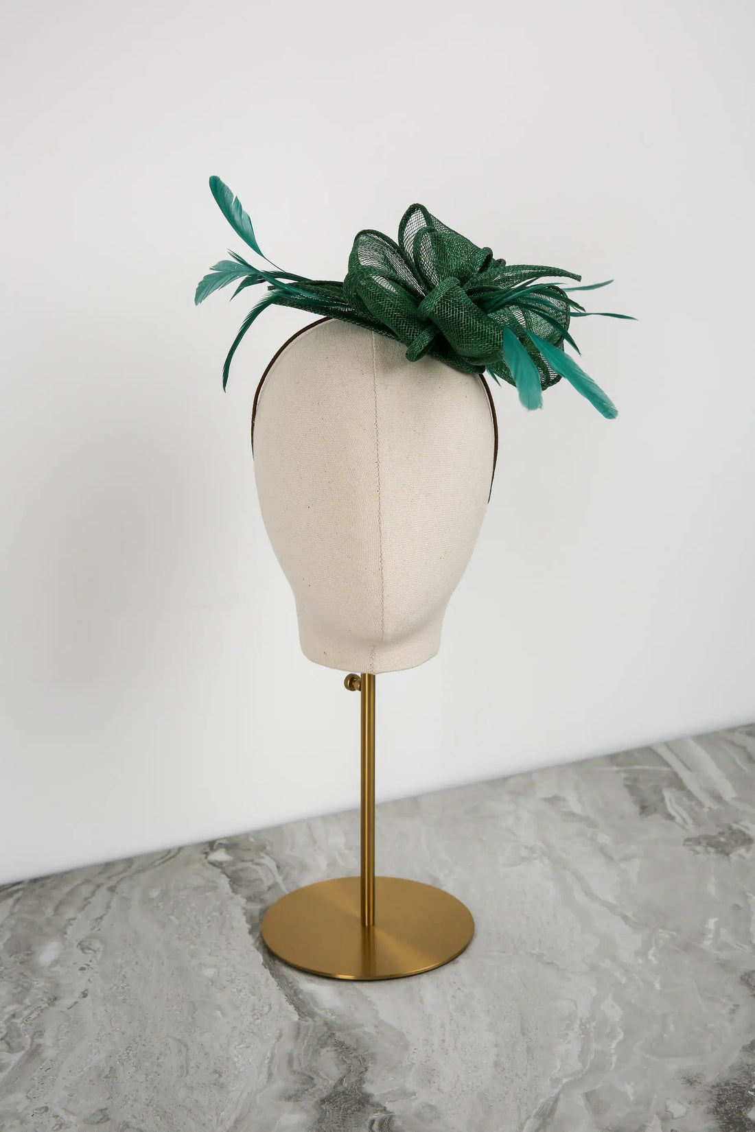 Green decorative fascinator on a mannequin head against a white background