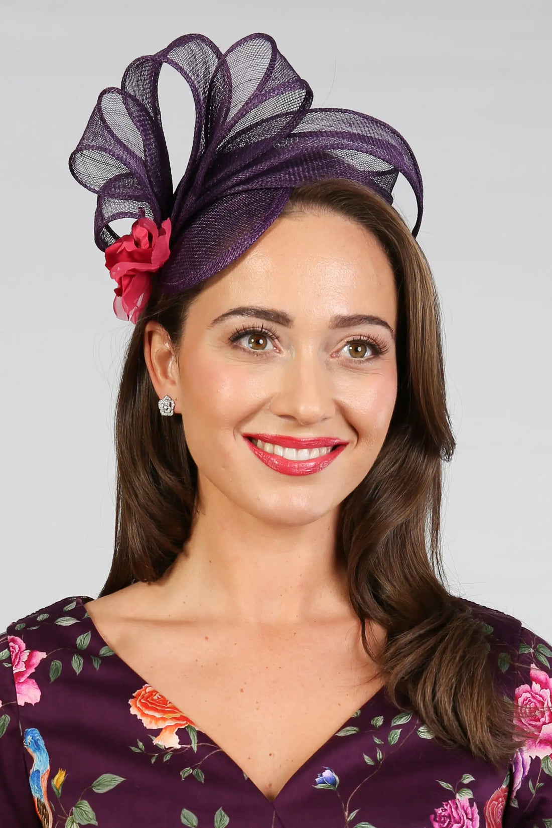 Woman wearing a blackberry coloured fascinator with a pink flower detail.