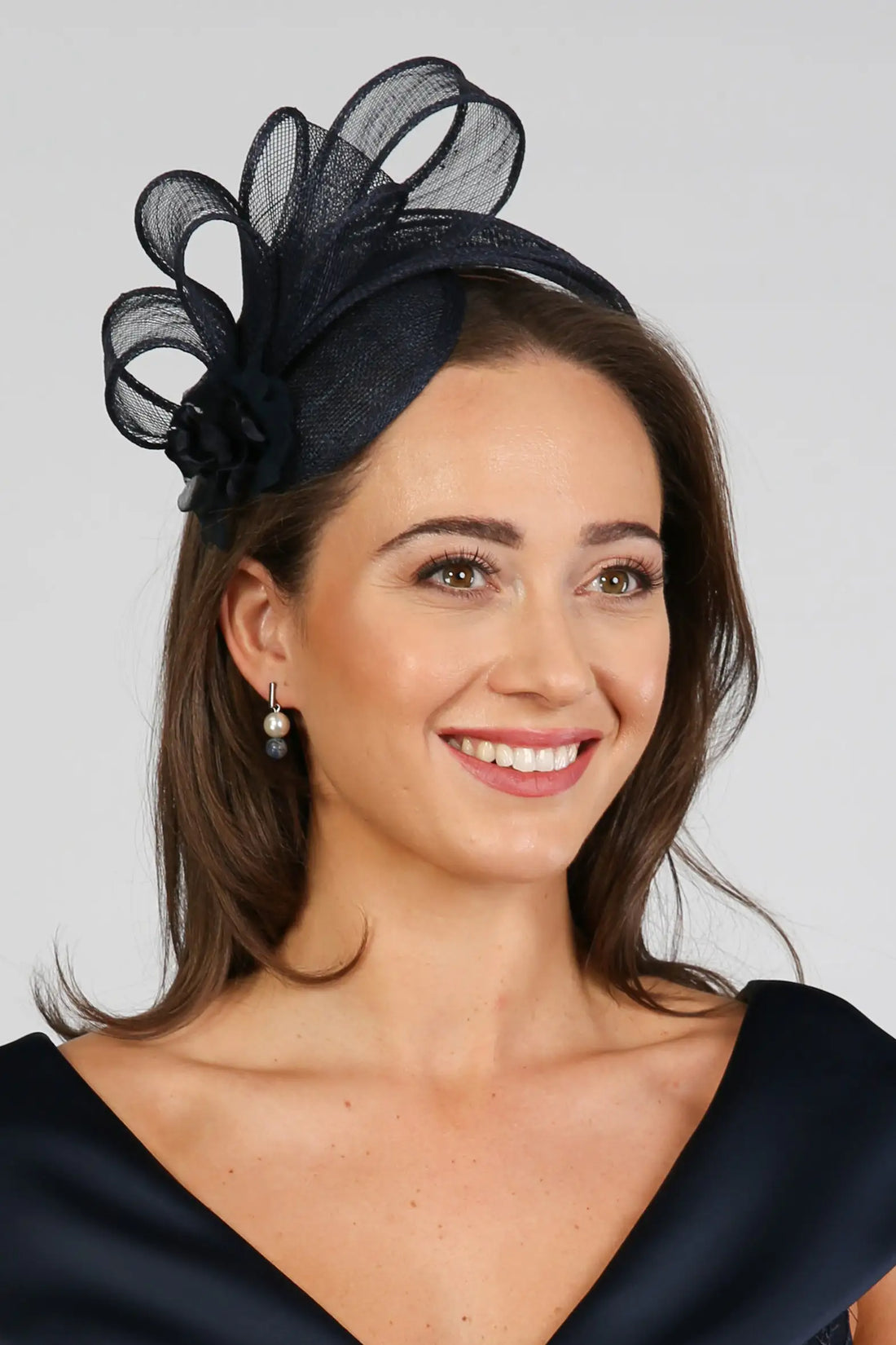 A woman wearing a navy fascinator with loops of sinamay and a small hand made flower to the right.
