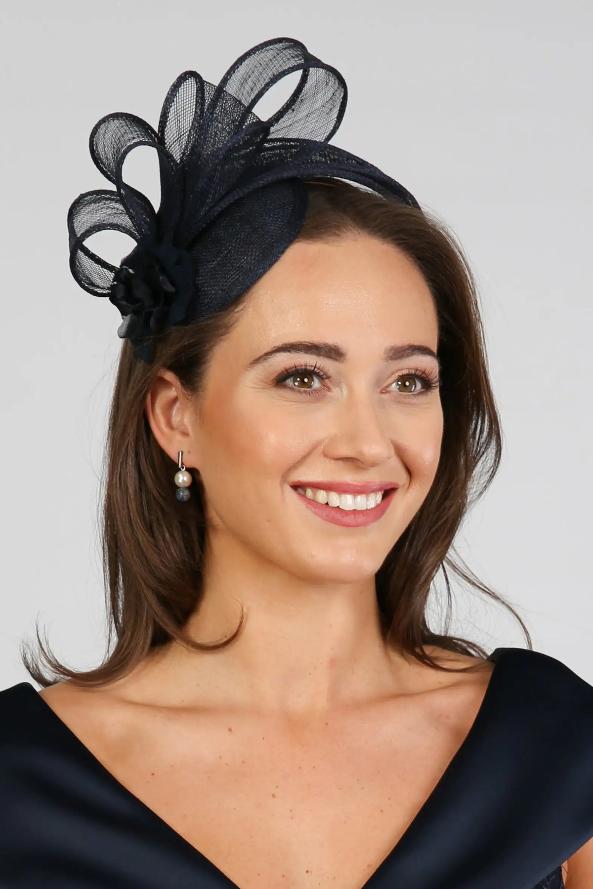 A woman wearing a navy fascinator with loops of sinamay and a small hand made flower to the right.