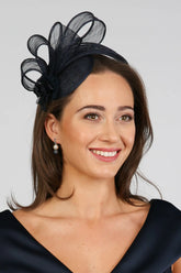 A woman wearing a navy fascinator with loops of sinamay and a small hand made flower to the right.