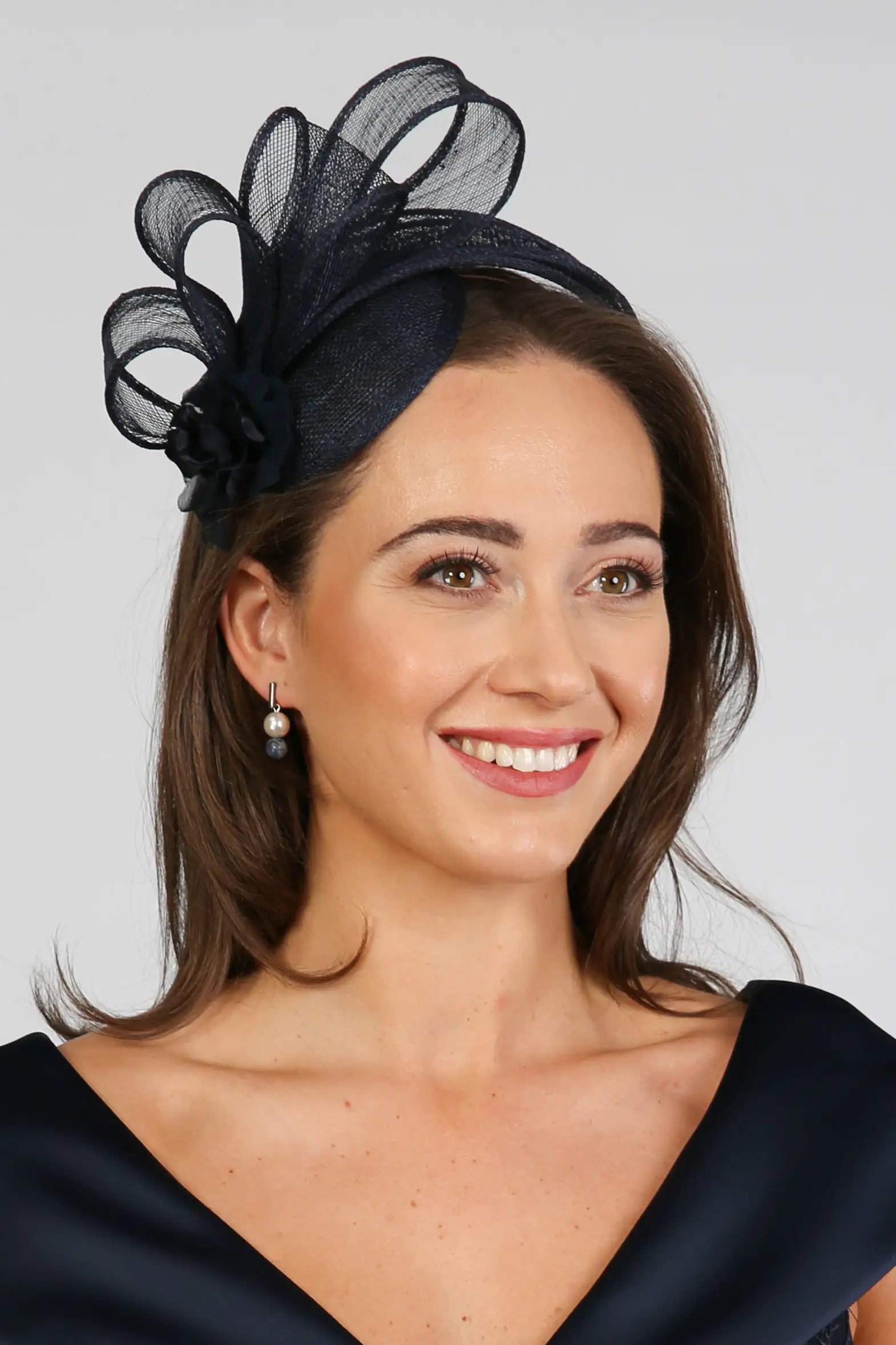 A woman wearing a navy fascinator with loops of sinamay and a small hand made flower to the right.