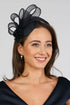 A woman wearing a navy fascinator with loops of sinamay and a small hand made flower to the right.