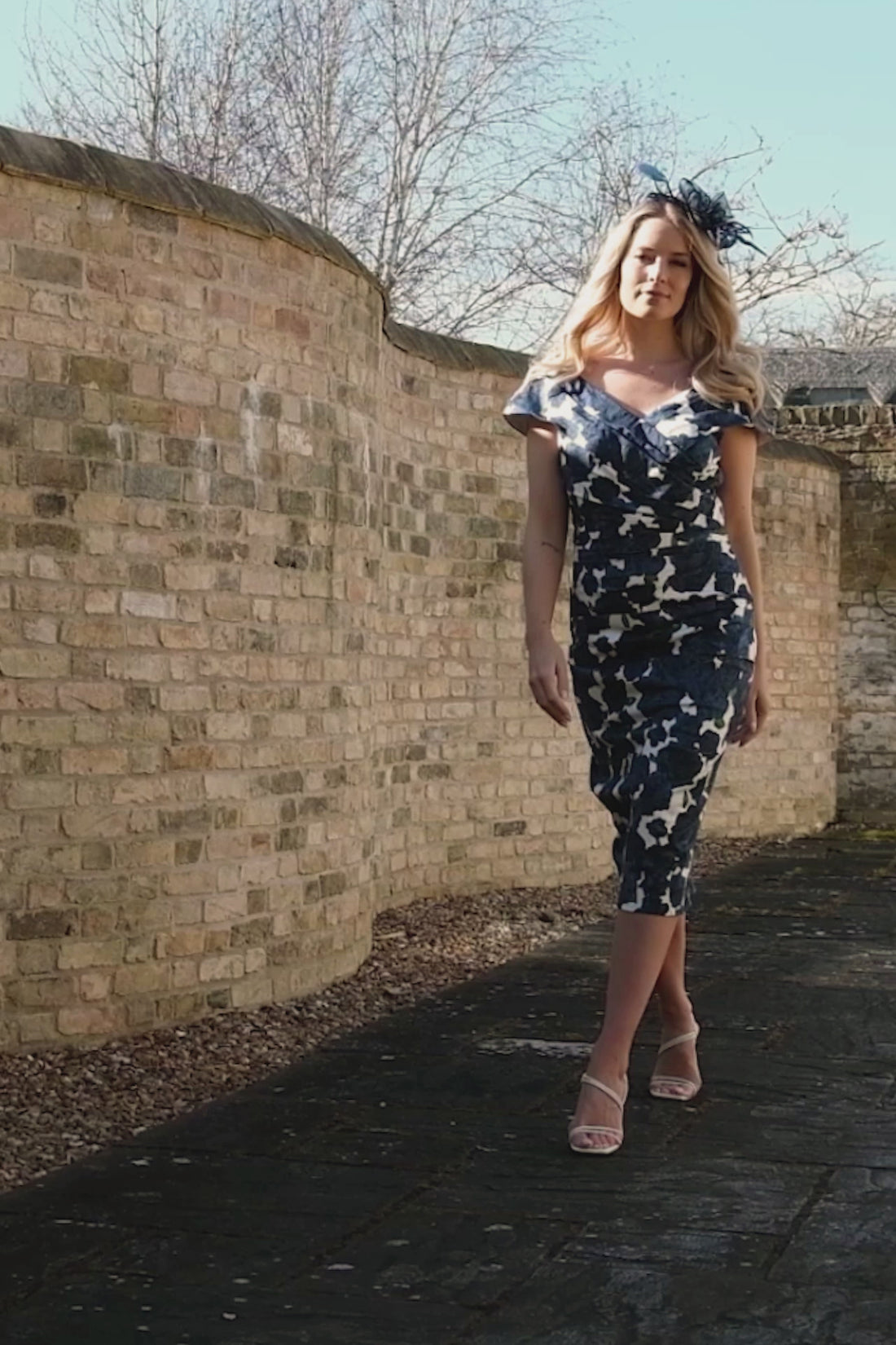 A woman wearing a navy roses print Bardot dress with short pleated sleeves and a fitted design.